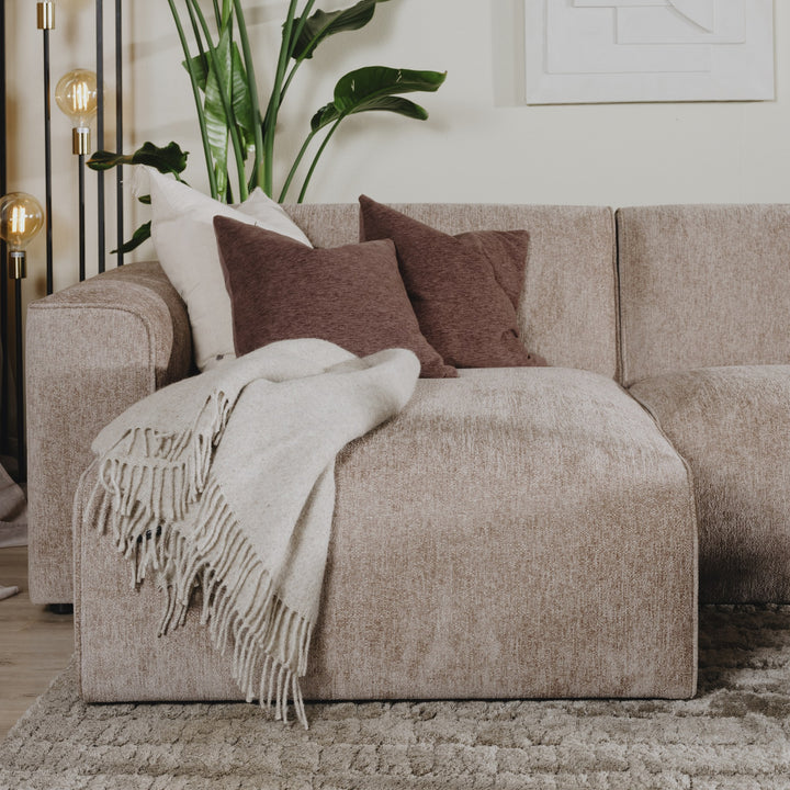 Como hjørnesofa i gråbeige chenille med brune puter og lyst pledd, plante og gulvlampe