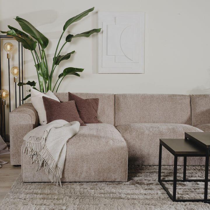 Como hjørnesofa i gråbeige chenille med brun pute og pledd, hvit veggkunst og plante