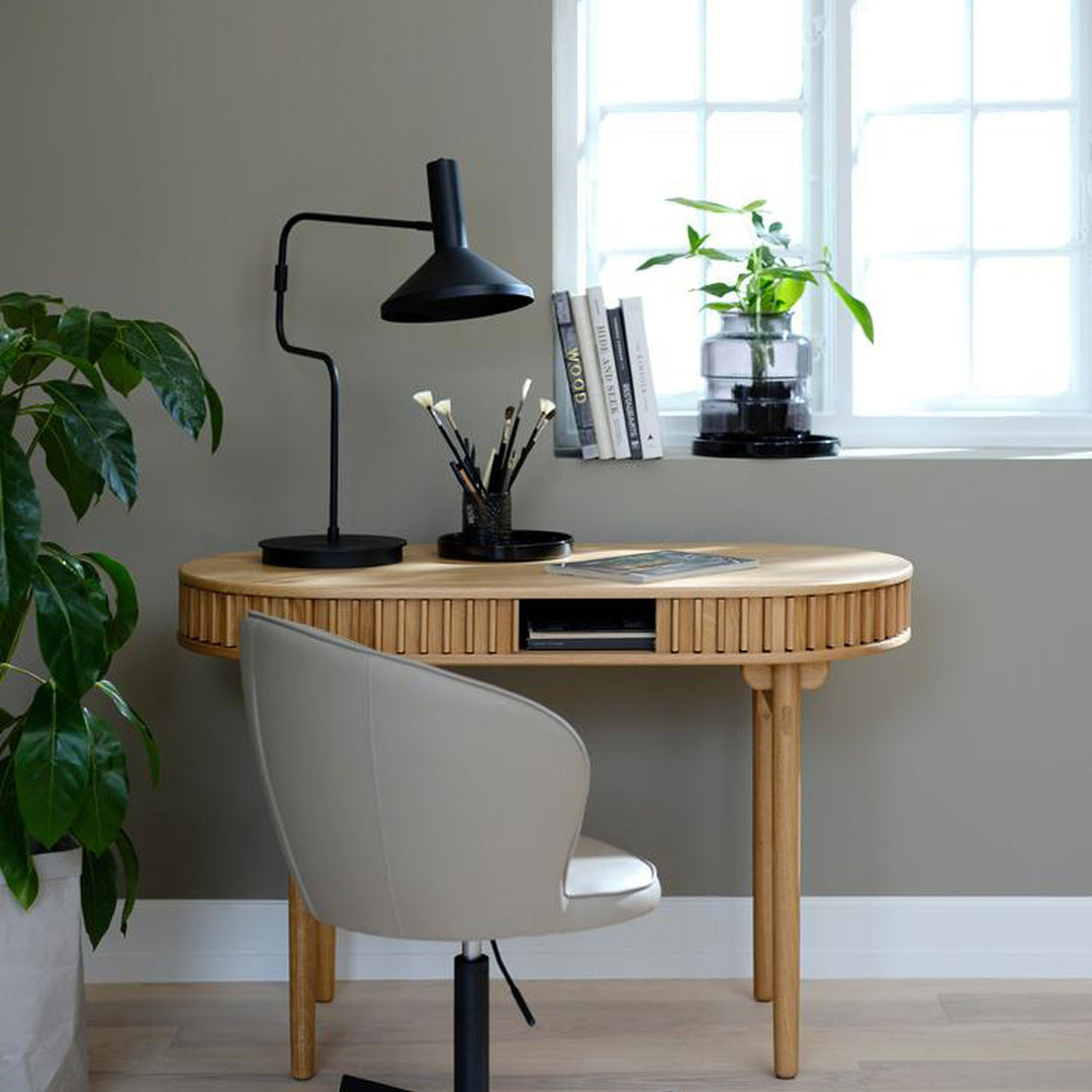 Carno skrivebord i eik med rillet front i rom med sort bordlampe, plante og hvit stol