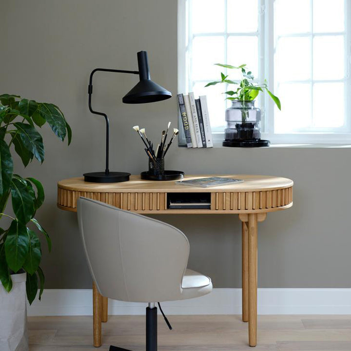 Carno skrivebord i eik med rillet front i rom med sort bordlampe, plante og hvit stol