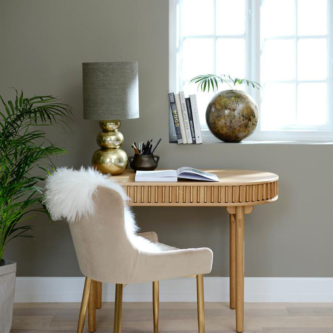 Carno skrivebord i eik med rillet front, beige velurstol, fåreskinn og messinglampe