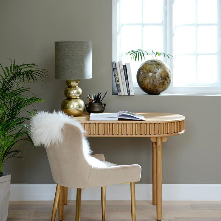 Carno skrivebord i eik med rillet front, beige velurstol, fåreskinn og messinglampe