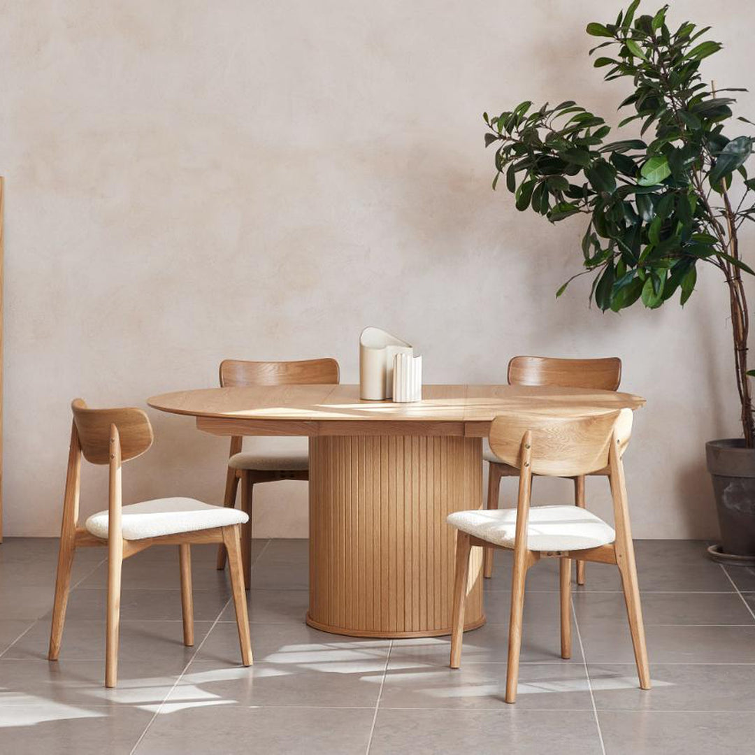 Fiola spisebord i natur eik, oval og uttrekt, med eikestoler, stor grønn plante og beige vegg