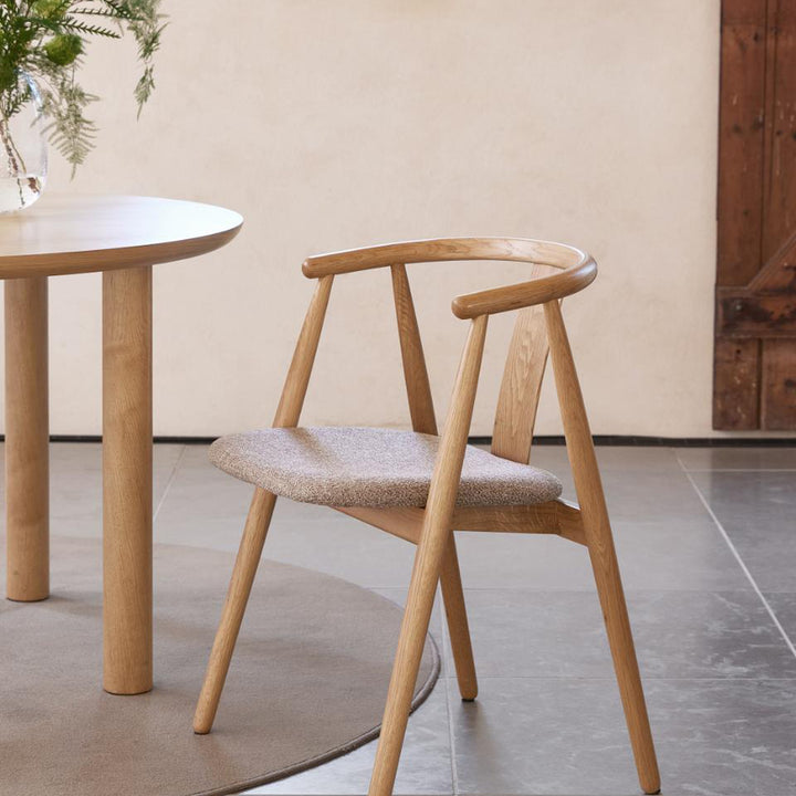 Relate spisestol i natur eik med lyst bouclé-sete, ved rundt eikebord mot beige vegg