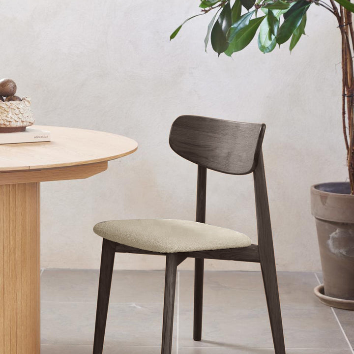 Elim spisestol i espressobrun eik med beige bouclé-sete, ved rundt eikebord mot beige vegg