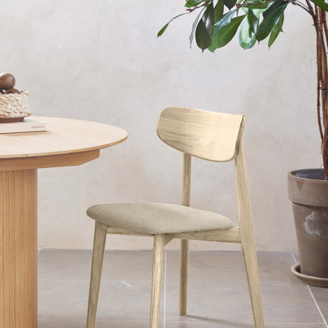 Elim spisestol i hvitoljet eik med beige bouclé-sete, ved rundt eikebord mot beige vegg
