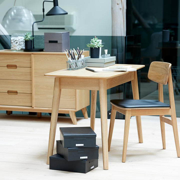 Livo spisestol i lys eik med sort kunstskinn ved eikeskrivebord med lampe og bokser