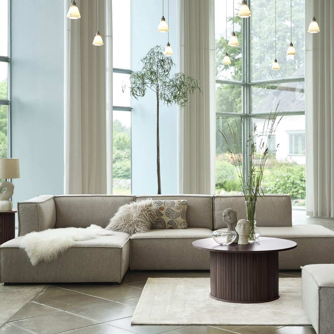 Fiola sofabord i espresso eik, rundt med riflet fot, foran beige sofa i lyst rom med store vinduer
