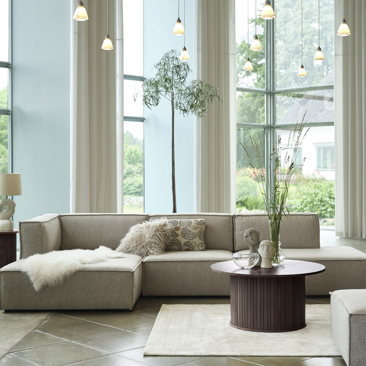 Fiola sofabord i espresso eik, rundt med riflet fot, foran beige sofa i lyst rom med store vinduer