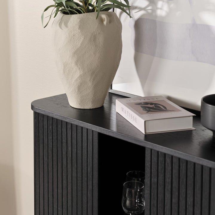 Cavo skap i sort eik, detalj av topp med lys vase, Matisse-bok og glass i åpent rom