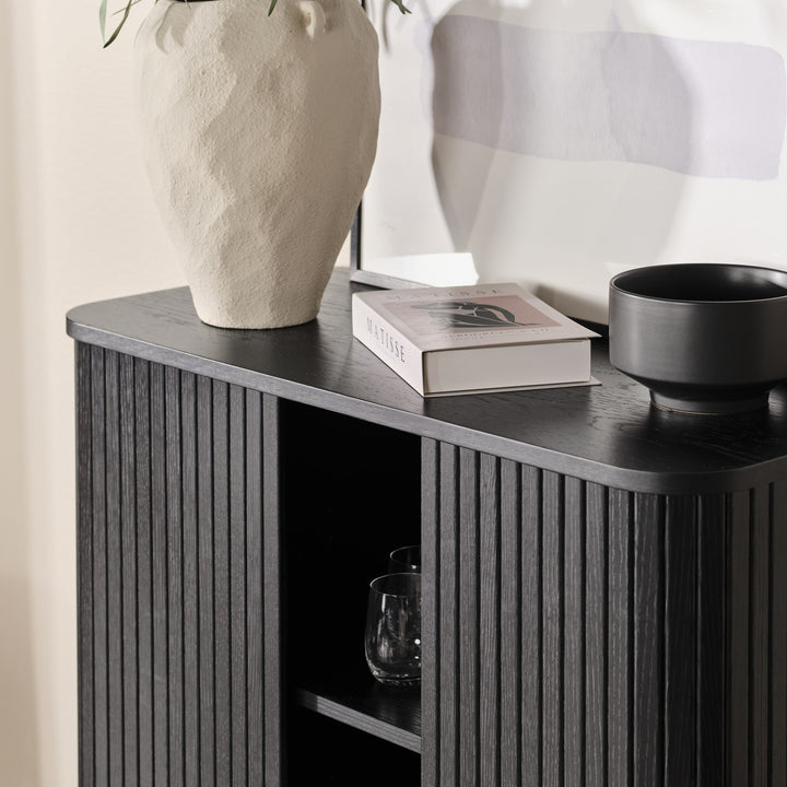 Cavo skap i sort eik, detalj av topp med lys vase, Matisse-bok, sort skål og glass i åpen seksjon