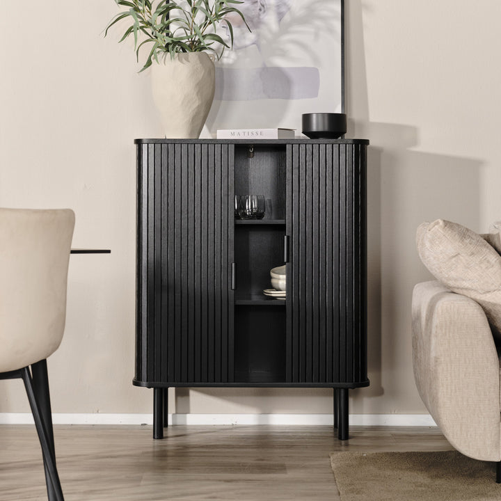 Cavo skap i sort eik med vertikale spiletredører, i beige rom med spisestol og lys sofa