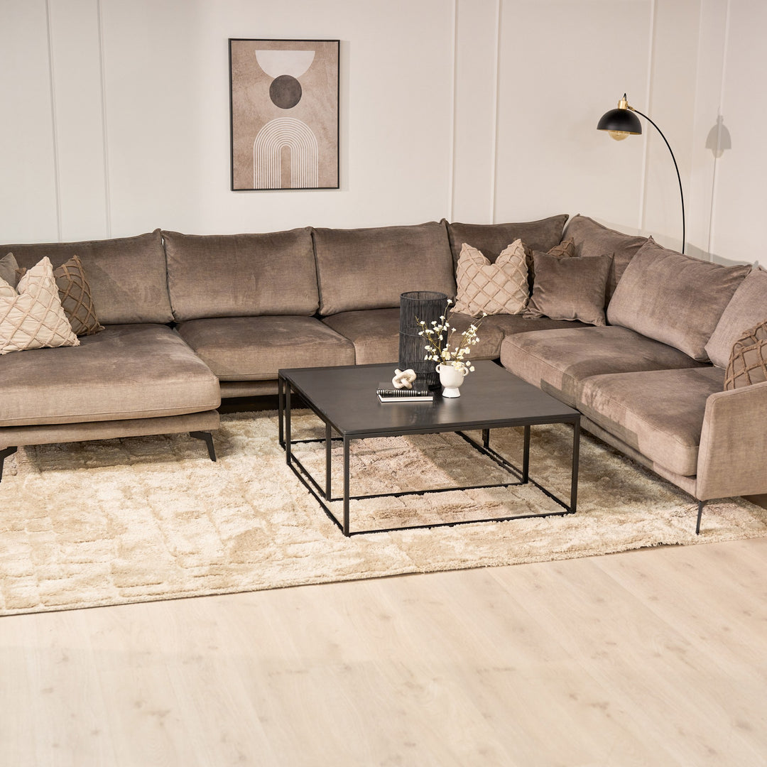 Bellus Coral hjørnesofa i gråbeige velur i stue med svart sofabord, teppe og veggkunst