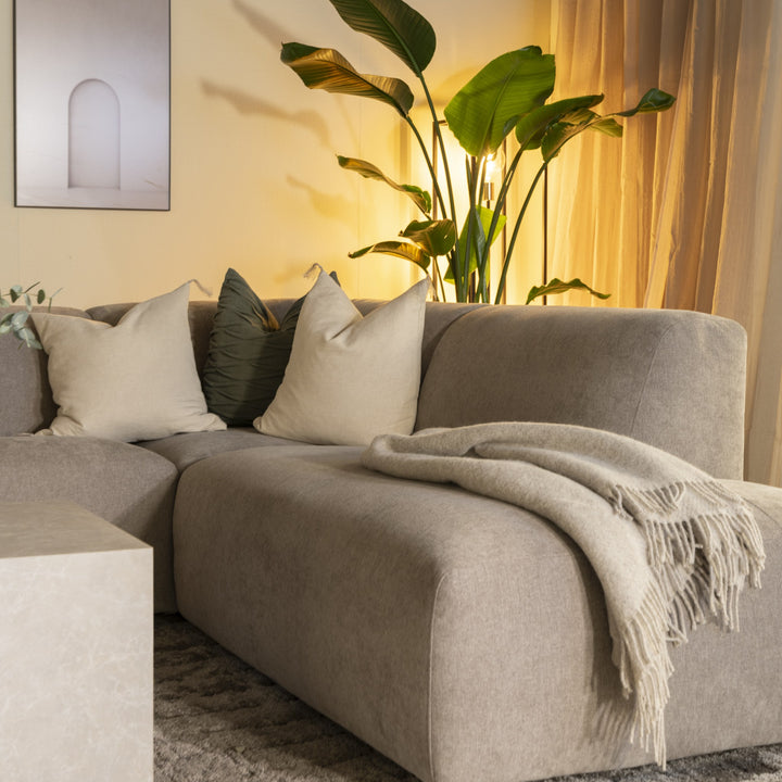 Bellus Olos hjørnesofa i lys grå chenille med pledd og puter, grønn plante i stue