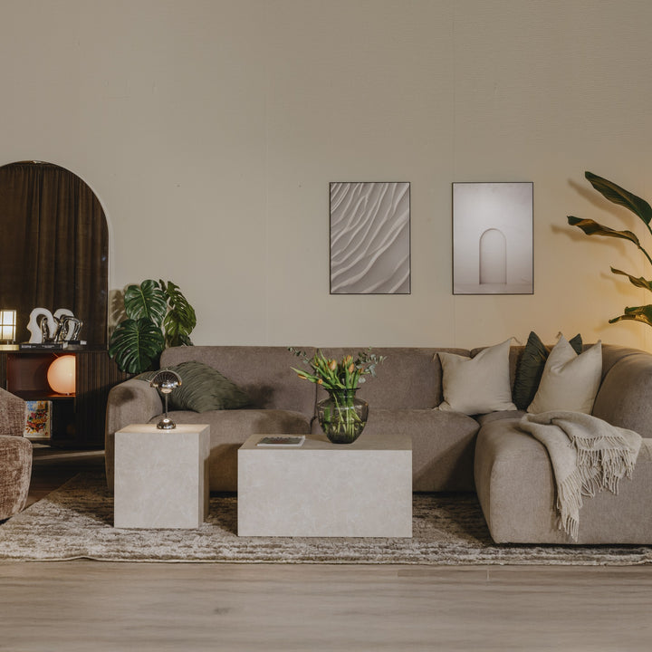 Bellus Olos hjørnesofa i beige stoff, høyrevendt, i stemningsbelyst rom med planter og lyse kubebord