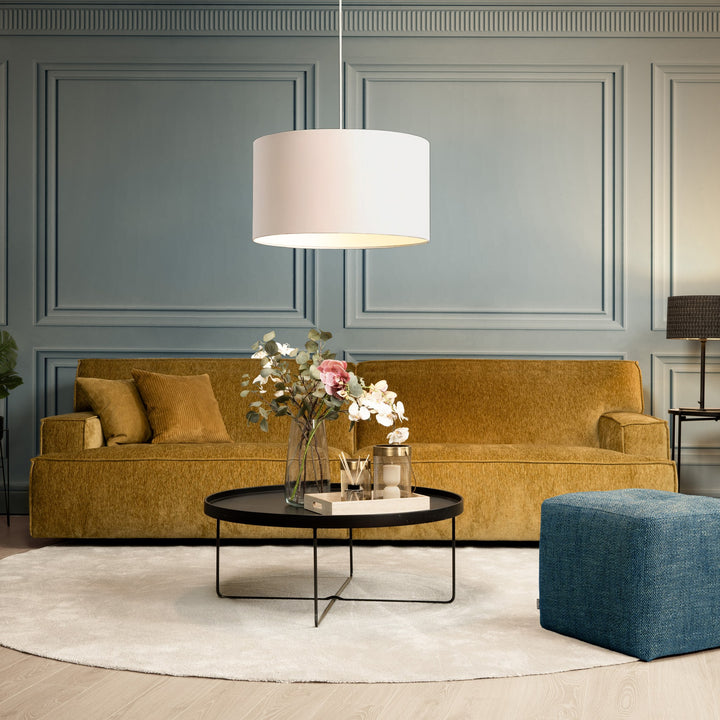 Bellus Mariposa 3-seter sofa i sennepsgul velur mot grå panelvegg med hvit taklampe og blå puff