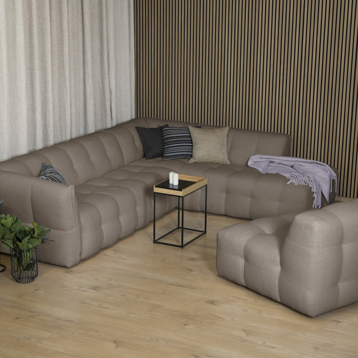 Bellus Moby sofa i gråbrun stoff med open end til høyre, mot mørk spilevegg med sidebord og grønn plante