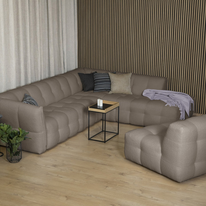 Bellus Moby sofa i gråbrun stoff med open end til høyre, mot mørk spilevegg med sidebord og grønn plante