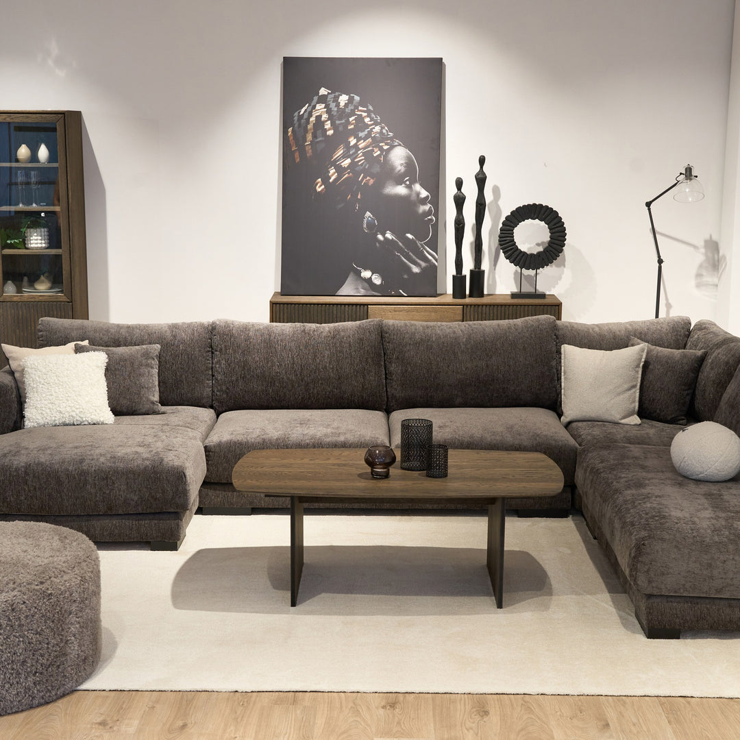 Bellus round puff i mørk grå chenille, foran stor grå hjørnesofa med ovalt trebord og veggbilde