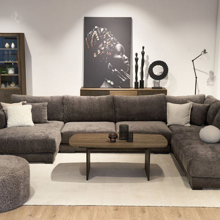 Bellus round puff i mørk grå chenille, foran stor grå hjørnesofa med ovalt trebord og veggbilde