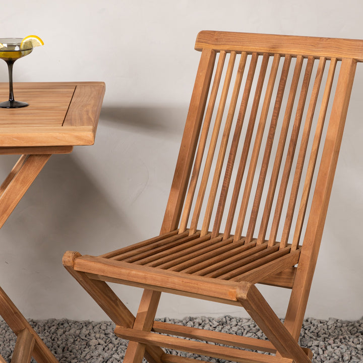 Venture Design Kenya klappstol i teak ved et lite bord på terrasse med grus