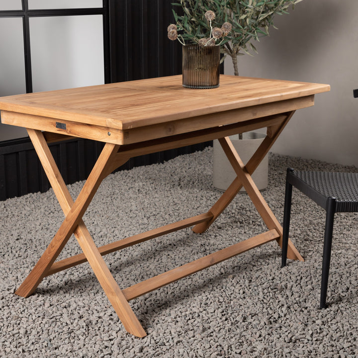 Venture Design Kenya spisebord i natur teak, sammenleggbart, på grått teppe ved sort vegg med plante