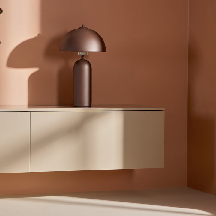 Frihamn tv-benk i beige med brun soppformet bordlampe mot terrakottavegg