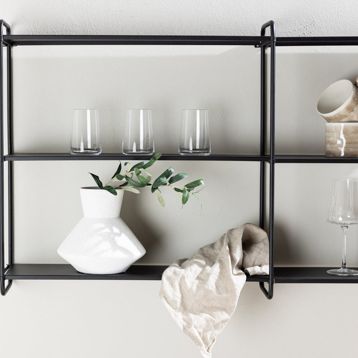 Lyon vegghylle i sort med hvit vase, glass og olivenkvist på lys vegg