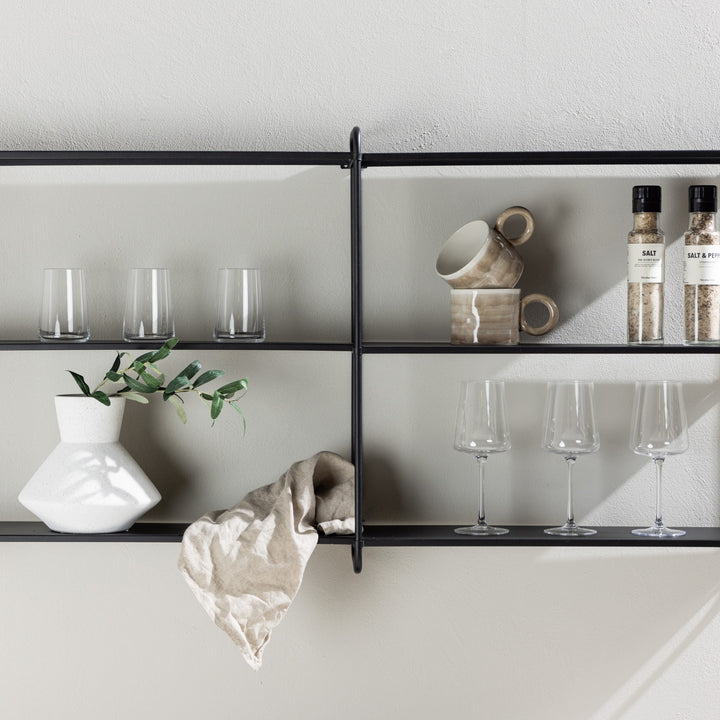 Lyon vegghylle i sort metall, bred modell med glass, krus og hvit vase mot lys vegg