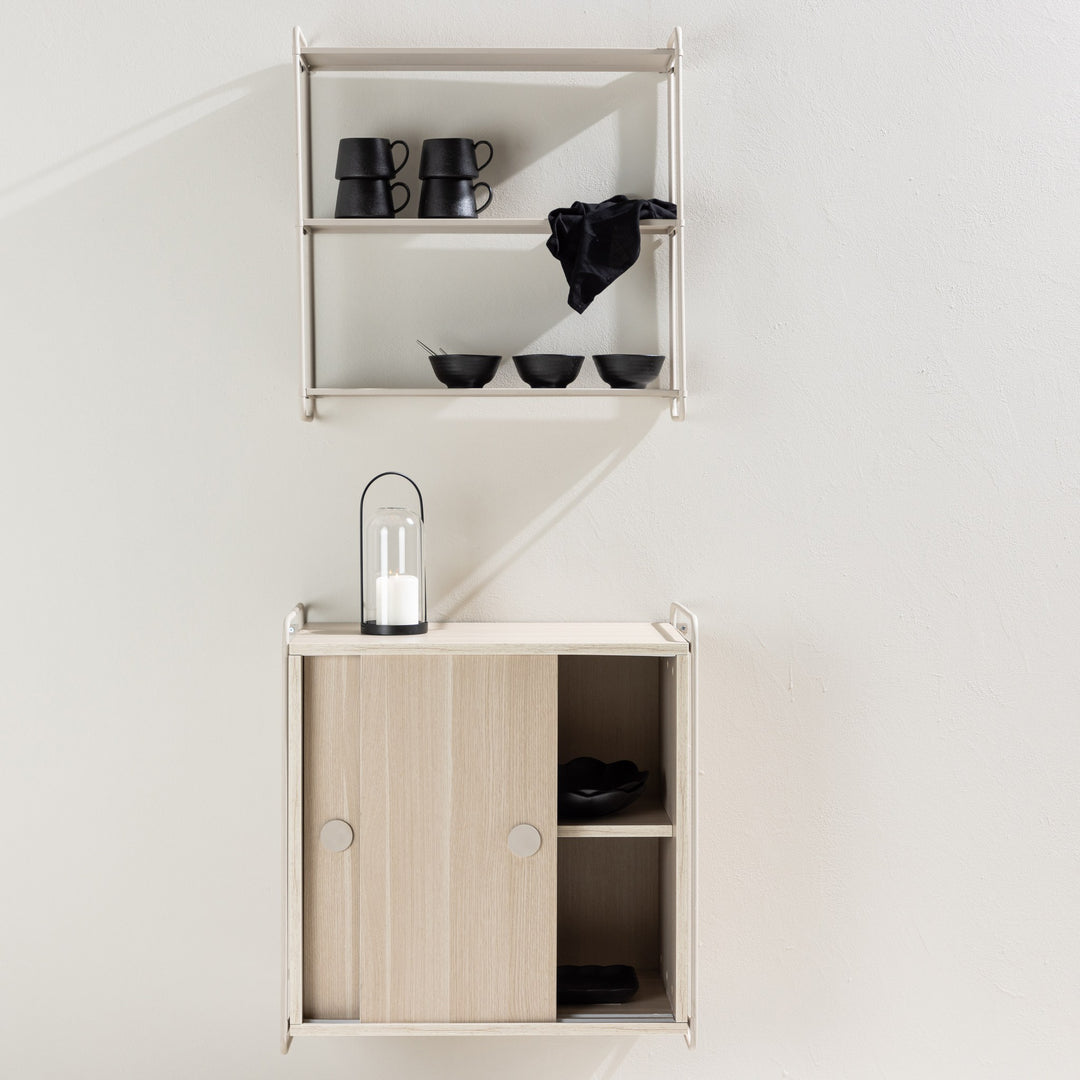 Lyon vegghylle i beige over lyst treskap med lanterne og levende lys i lyst rom