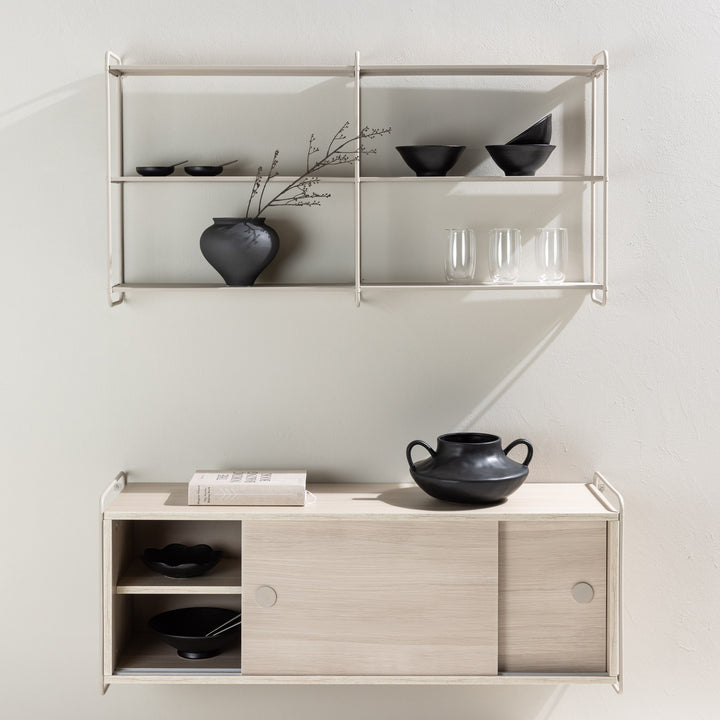 Lyon vegghylle i beige stylet med sorte boller, vase og glass, over lyst treskap