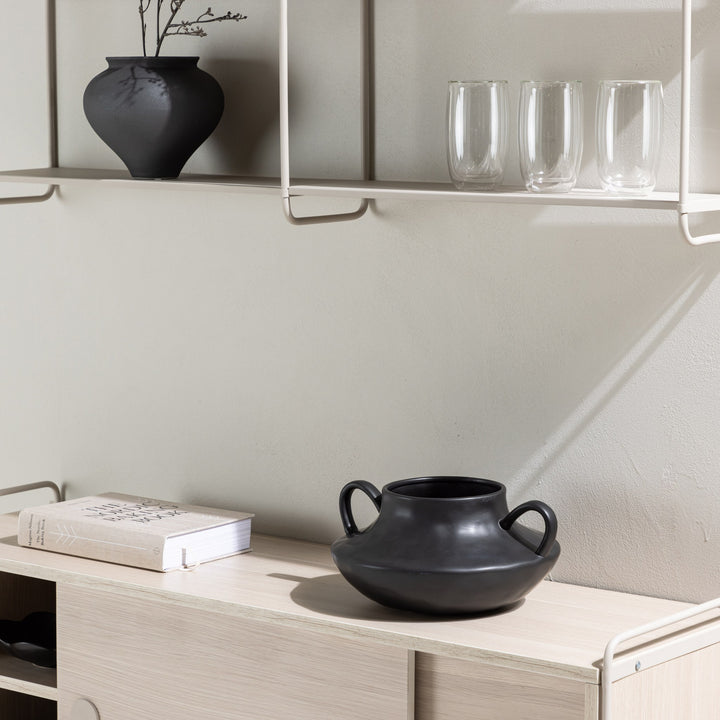 Lyon vegghylle i beige med sort vase og glass, over lyst treskap med sort krukke
