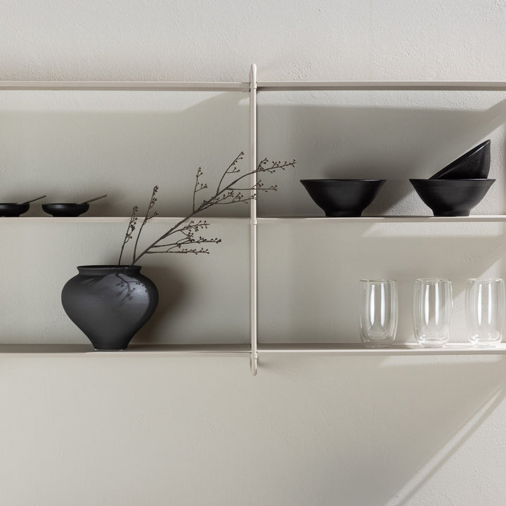Lyon vegghylle i beige metall, bred modell med sort vase, skåler og glass mot lys vegg