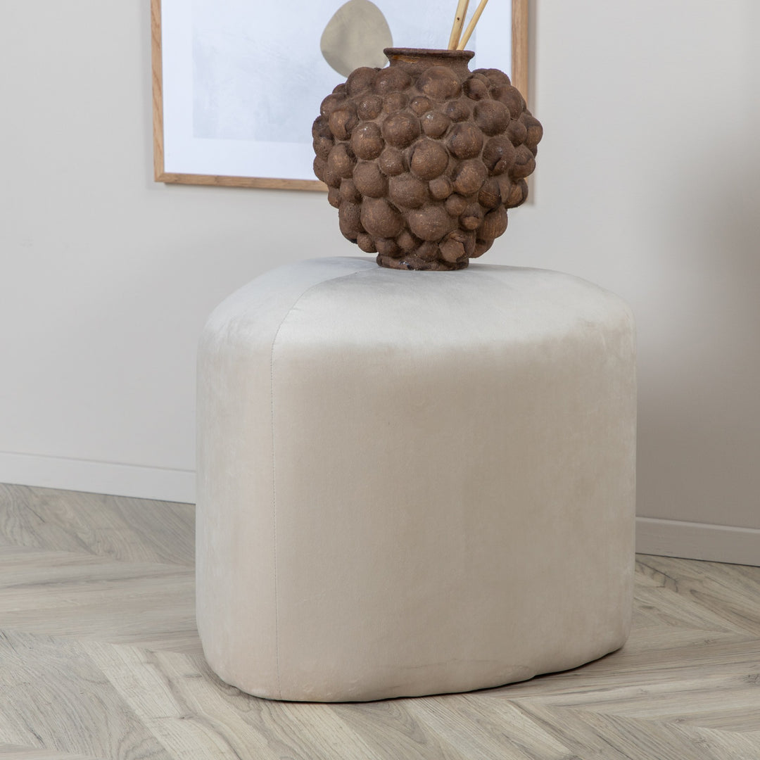 Peg puff i kremhvit velur med brun vase, lyst rom med fiskebensparkett
