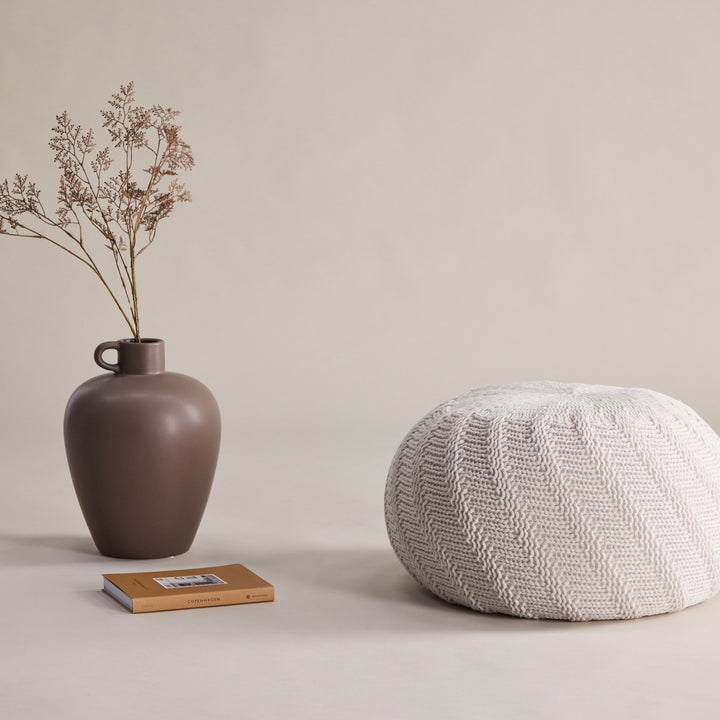 Ted puff rund i offwhite strikk, ved brun vase med tørrblomster og bok
