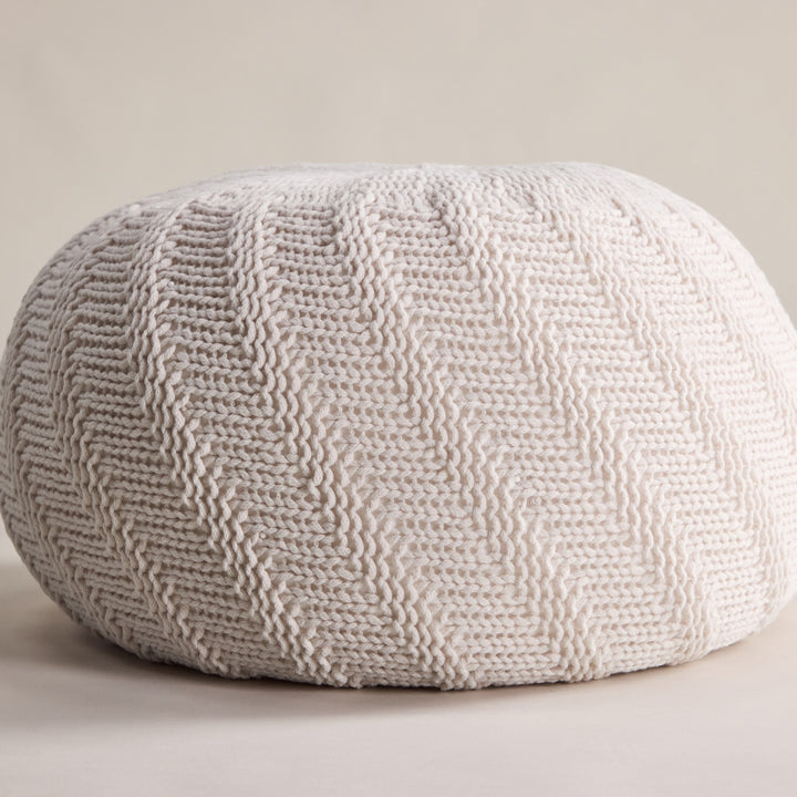 Ted puff i offwhite, rund strikket puff mot beige bakgrunn.