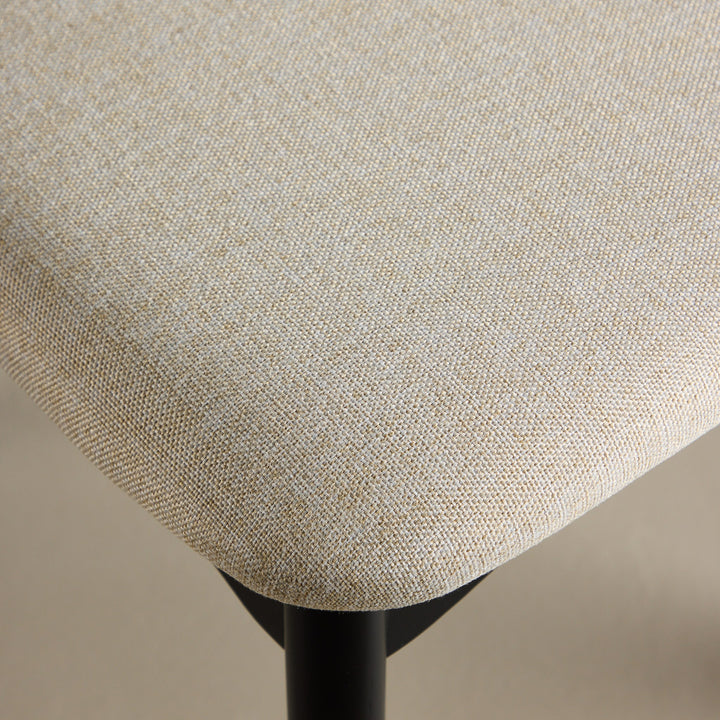 Ven spisestol, nærbilde av beige stofftrekk på sete med sort metallben