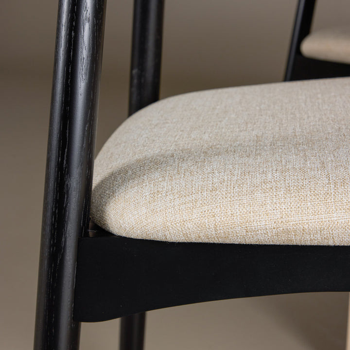 Ven spisestol med beige stoff på sete og sortmalt ramme, sett tett på