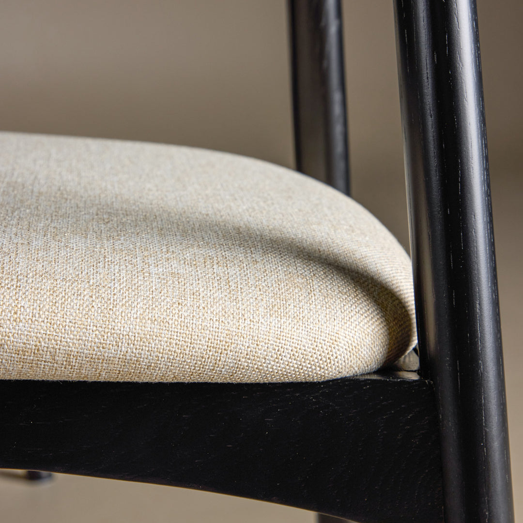 Ven spisestol i sort eik med beige stoffsete, nærbilde av sete og ben.