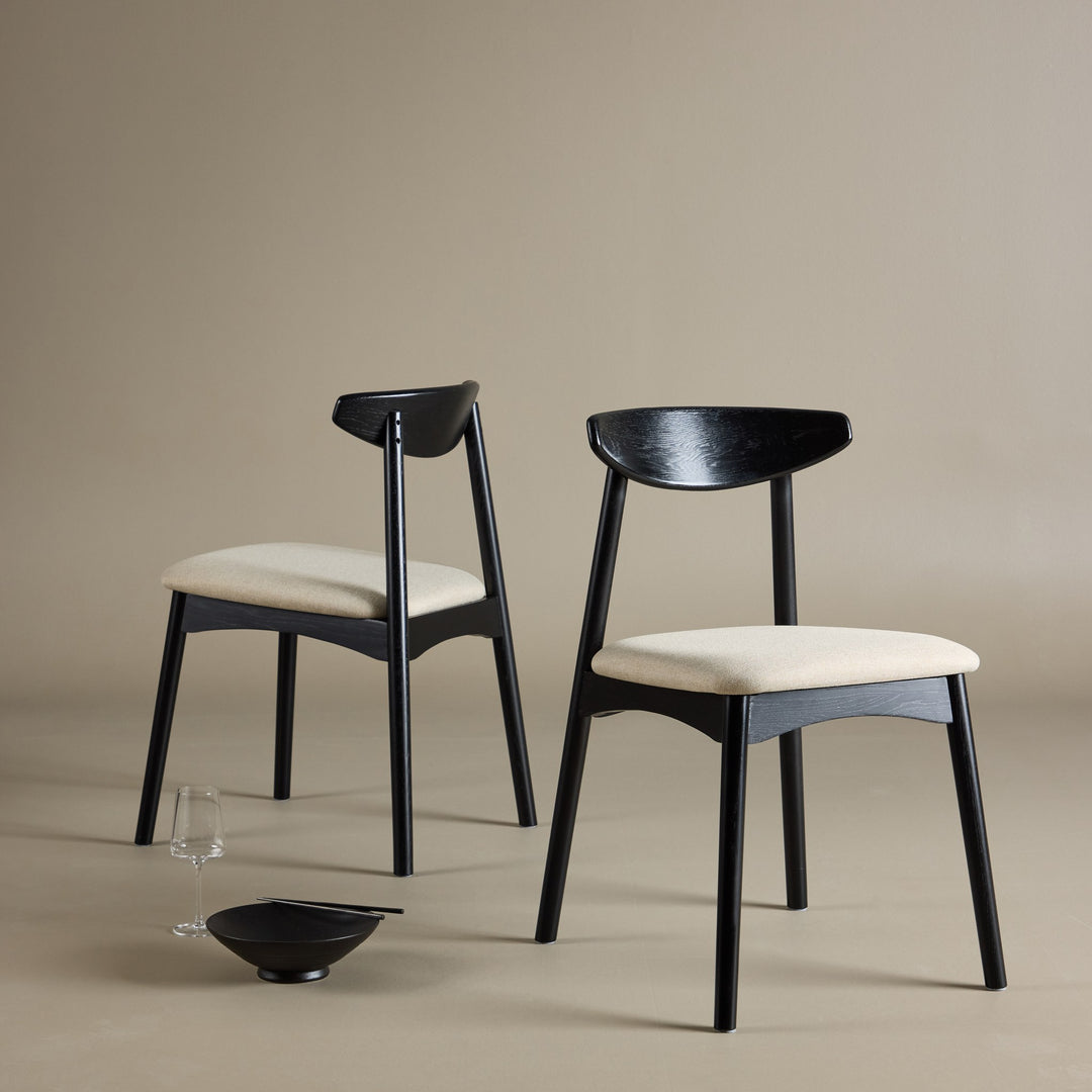 To Ven spisestoler i sort eik med beige seter, dekorert med skål og glass.