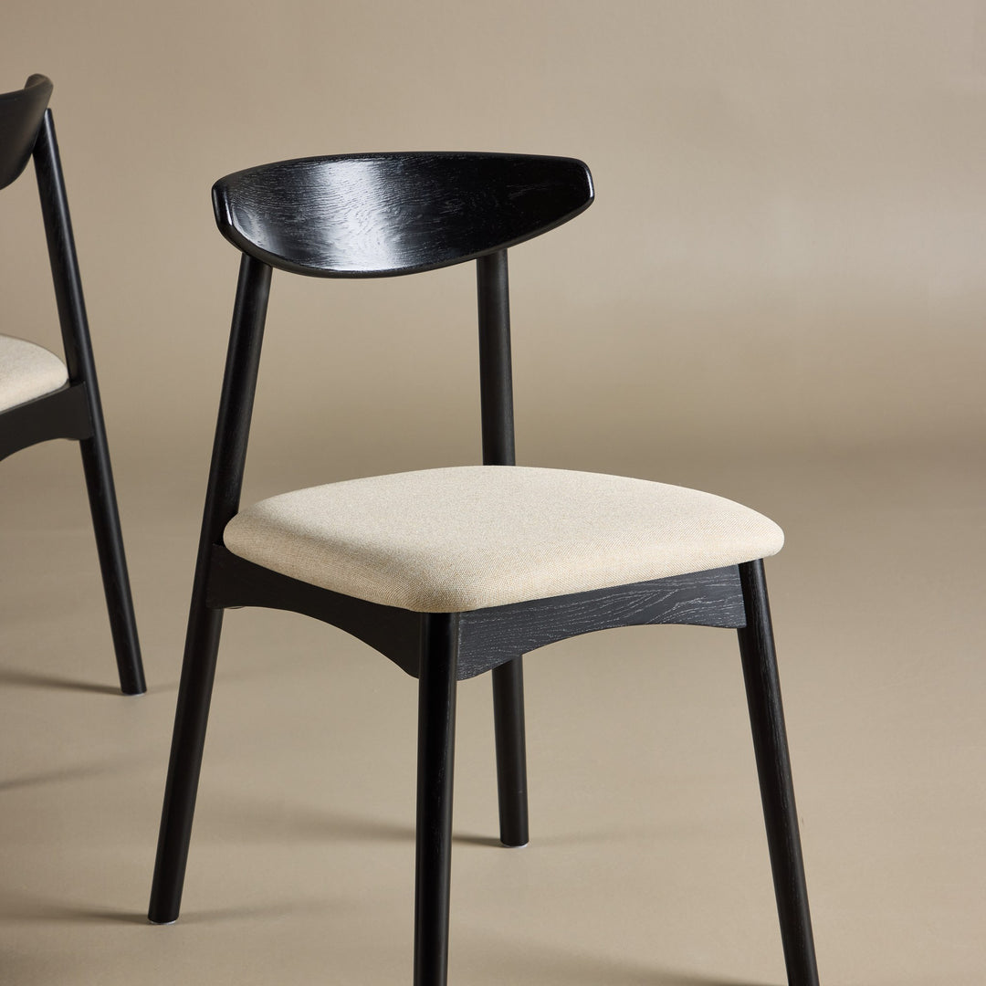 Ven spisestol i sort tre med beige stoffsete, mot beige bakgrunn