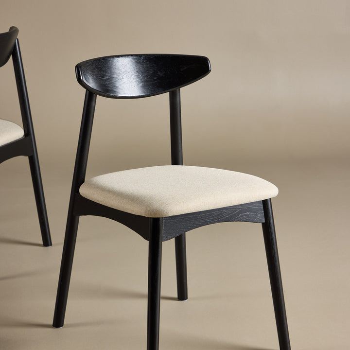 Ven spisestol i sort tre med beige stoffsete, mot beige bakgrunn