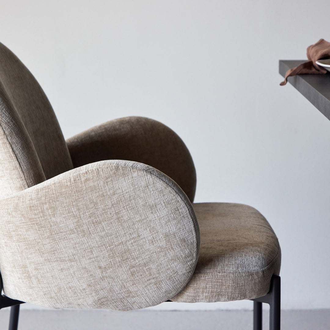 Blom spisestol i beige chenille, nærbilde av avrundet rygg ved mørkt bord.