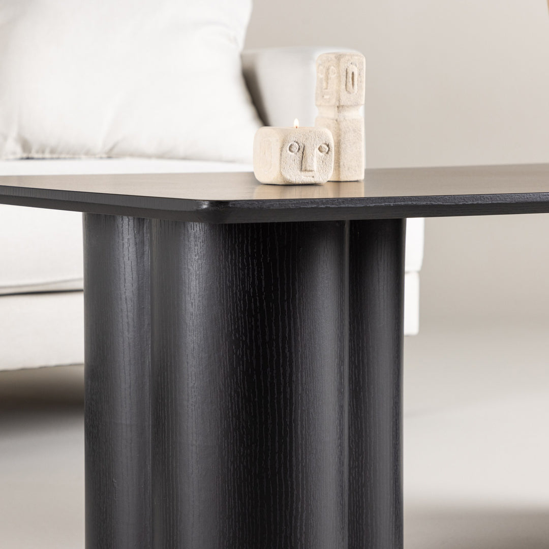 Olivia sofabord i sort, nærbilde av platen med to beige lysestaker formet som ansikter, hvit sofa bak
