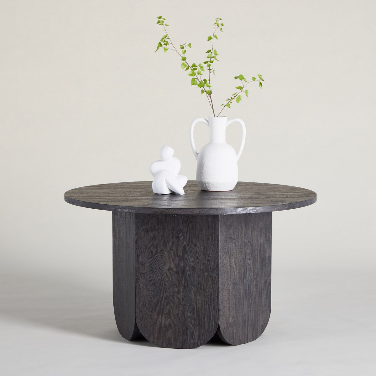 Tekla sofabord i sort, rundt med buet base, hvit skulptur og vase med grønne grener