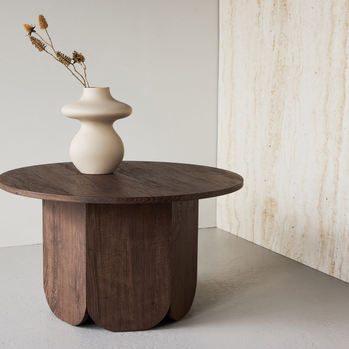 Tekla sofabord i mocca, rundt med buet søyleben og beige vase med tørket pryd