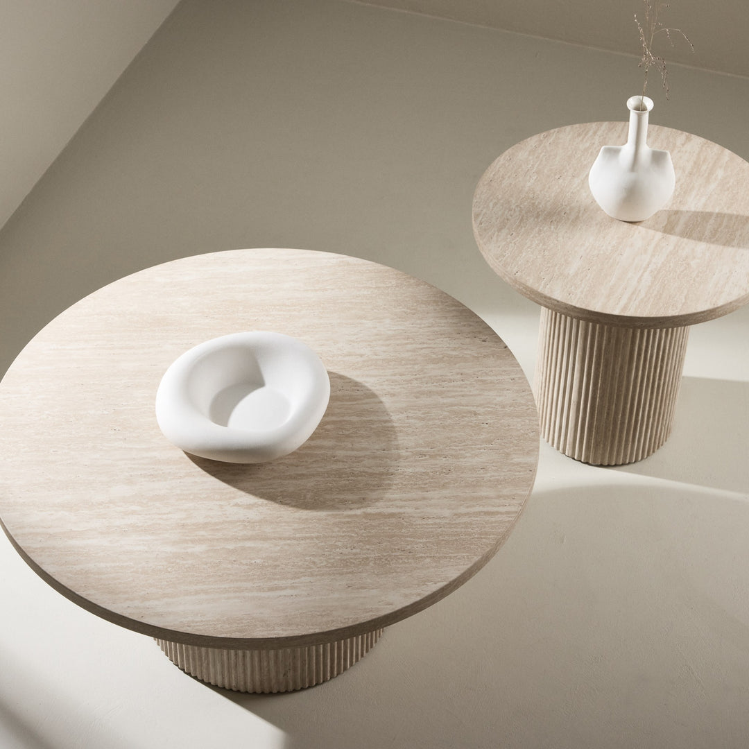 Harøn sidebord i lys travertin med hvit skål og vase, sett ovenfra i lyst rom med beige vegg