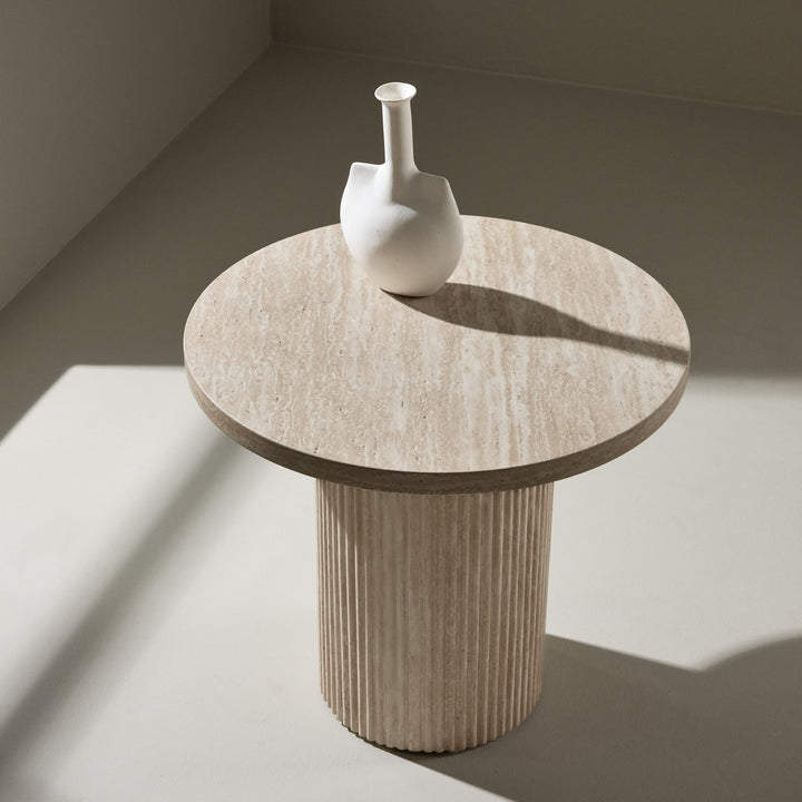 Harøn sidebord i lys travertin med riflet søylefot og hvit vase, i lyst rom med beige vegg