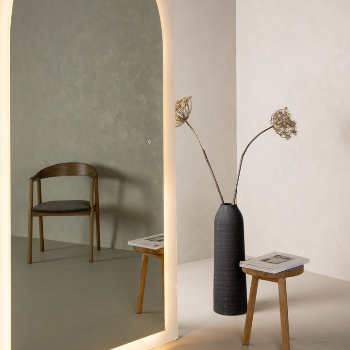 Skeppsvik speil med varmt LED-kantlys, speiler trestol mot salviegrønn vegg, ved vase med tørrblomster
