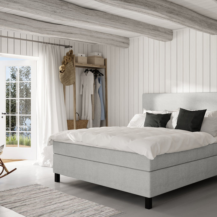 Wonderland W50 sengegavl i lys grå, oppredd seng i lyst panelt soverom med klesstativ og teppe